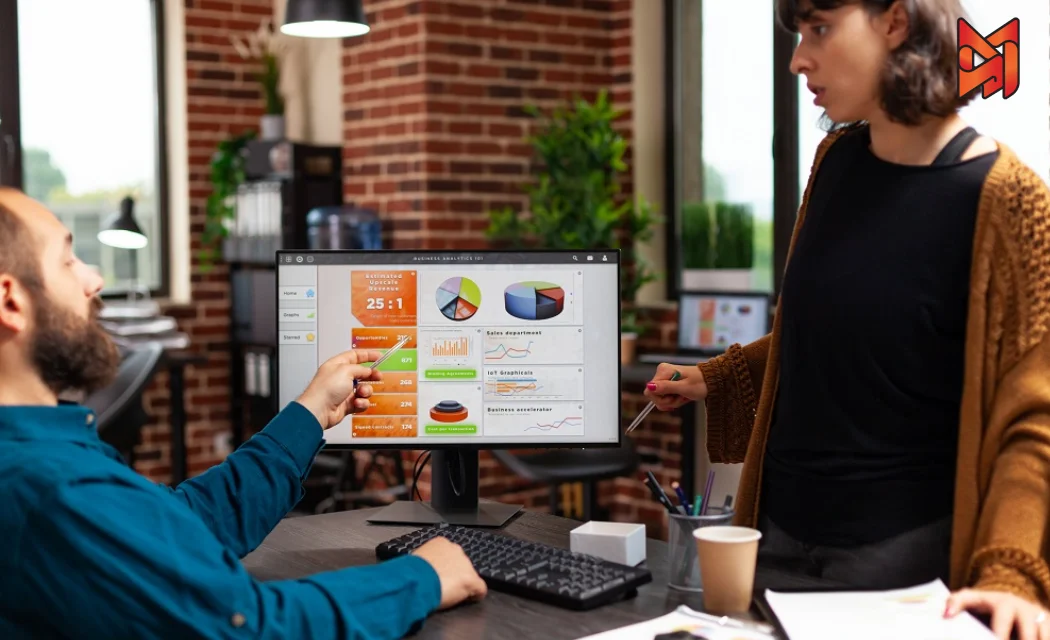 Two coworkers analyzing a graph of marketing performance metrics on a monitor.