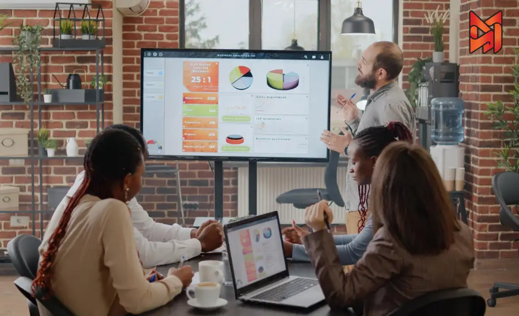 A digital marketing team brainstorms strategies in front of a large screen displaying campaign results.