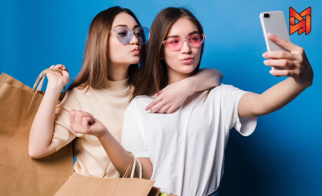 Two Gen Z girls with shopping bags taking a selfie, showcasing their happiness from shopping online.